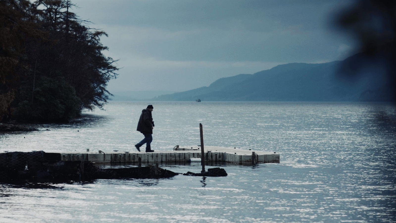 Man walking on a jetty in the middle of a loch in Inverness. Still from Loch Ness: They Created a Monster, courtesy of The Scottish Documentary Institute